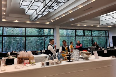 Entrée d'un bâtiment blanc entouré d'arbres, avec des portes vitrées illuminées par une lumière intérieure.