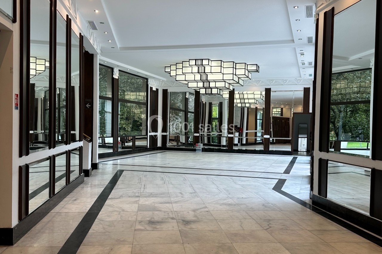 Hall lumineux avec sol en marbre, miroirs muraux, grandes fenêtres et un lustre géométrique suspendu.