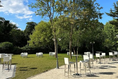 Entrée d'un bâtiment blanc entouré d'arbres, avec des portes vitrées illuminées par une lumière intérieure.