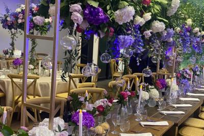 Table dressée avec des chaises transparentes, ornée de compositions florales tropicales colorées et de bougies.