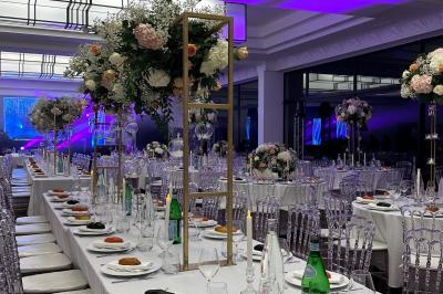 Table dressée avec des chaises transparentes, ornée de compositions florales tropicales colorées et de bougies.