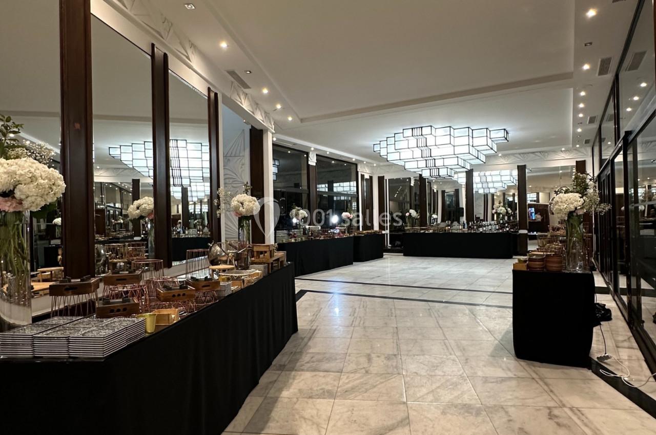Salle élégante avec tables de buffet alignées, décorée de fleurs blanches et éclairée par un grand lustre moderne.