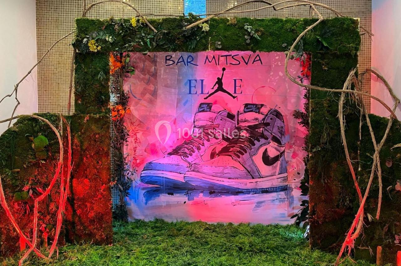 Décor de bar-mitsva avec des baskets illustrées, entouré de mousse, branches et éclairages colorés.