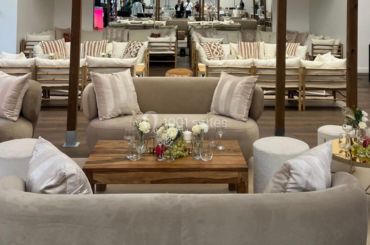 Espace lounge avec canapés beiges, table basse en bois décorée de fleurs blanches et verres, ambiance conviviale.