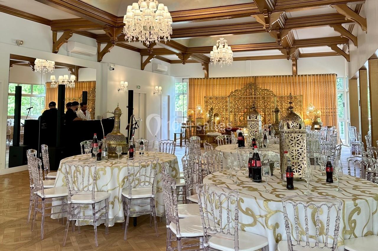 Salle de réception élégante avec tables décorées, chaises transparentes et lustres, dans un cadre lumineux et raffiné.