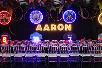 Table dressée avec des chaises transparentes, ornée de compositions florales tropicales colorées et de bougies.