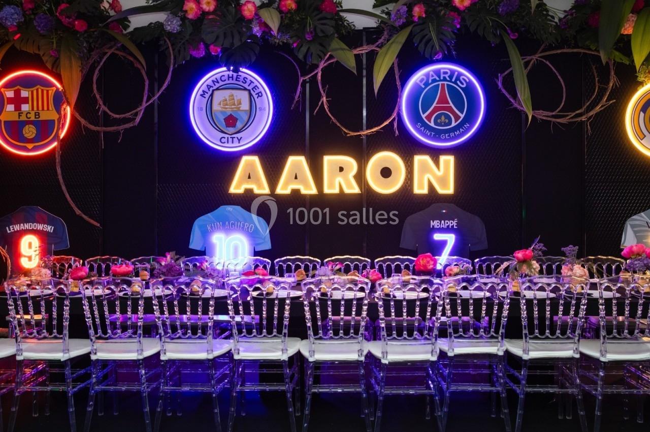 Table décorée avec des chaises transparentes, devant des maillots de football et des logos de clubs illuminés.