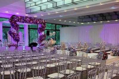 Table dressée avec des chaises transparentes, ornée de compositions florales tropicales colorées et de bougies.