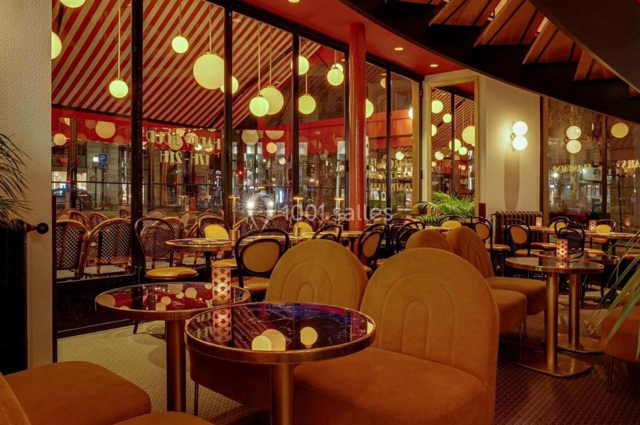 Intérieur d'un café avec des tables rondes, des fauteuils jaunes, des lumières suspendues et une grande baie vitrée.