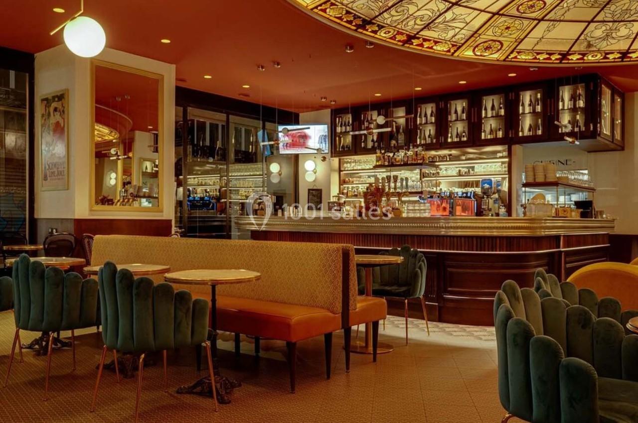 Intérieur d'un café élégant avec un bar en bois, des banquettes colorées et un plafond décoratif lumineux.
