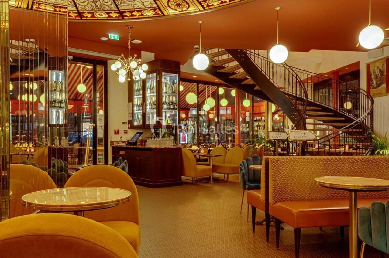 Intérieur d'un café élégant avec des tables rondes, des banquettes colorées et un escalier en colimaçon.