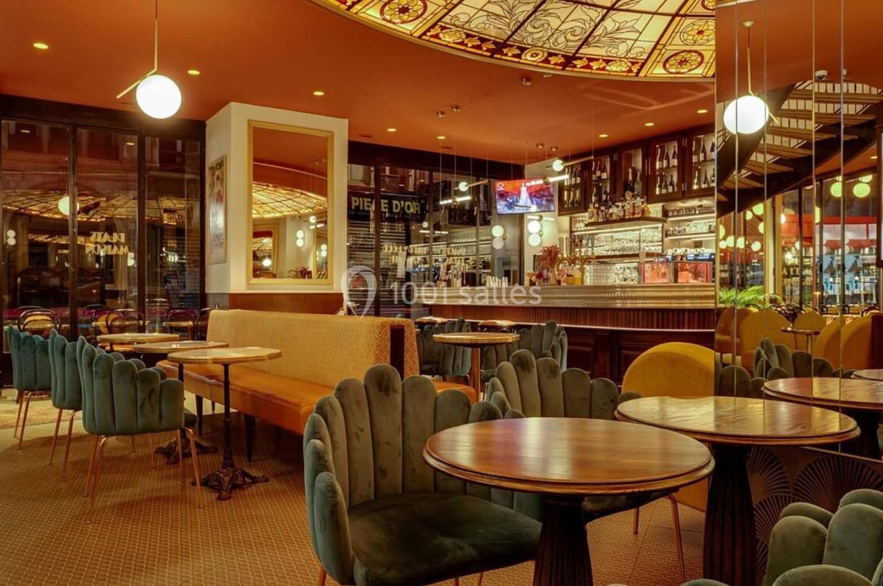 Intérieur d'un café élégant avec tables rondes, chaises colorées, bar en arrière-plan et plafond décoratif lumineux.