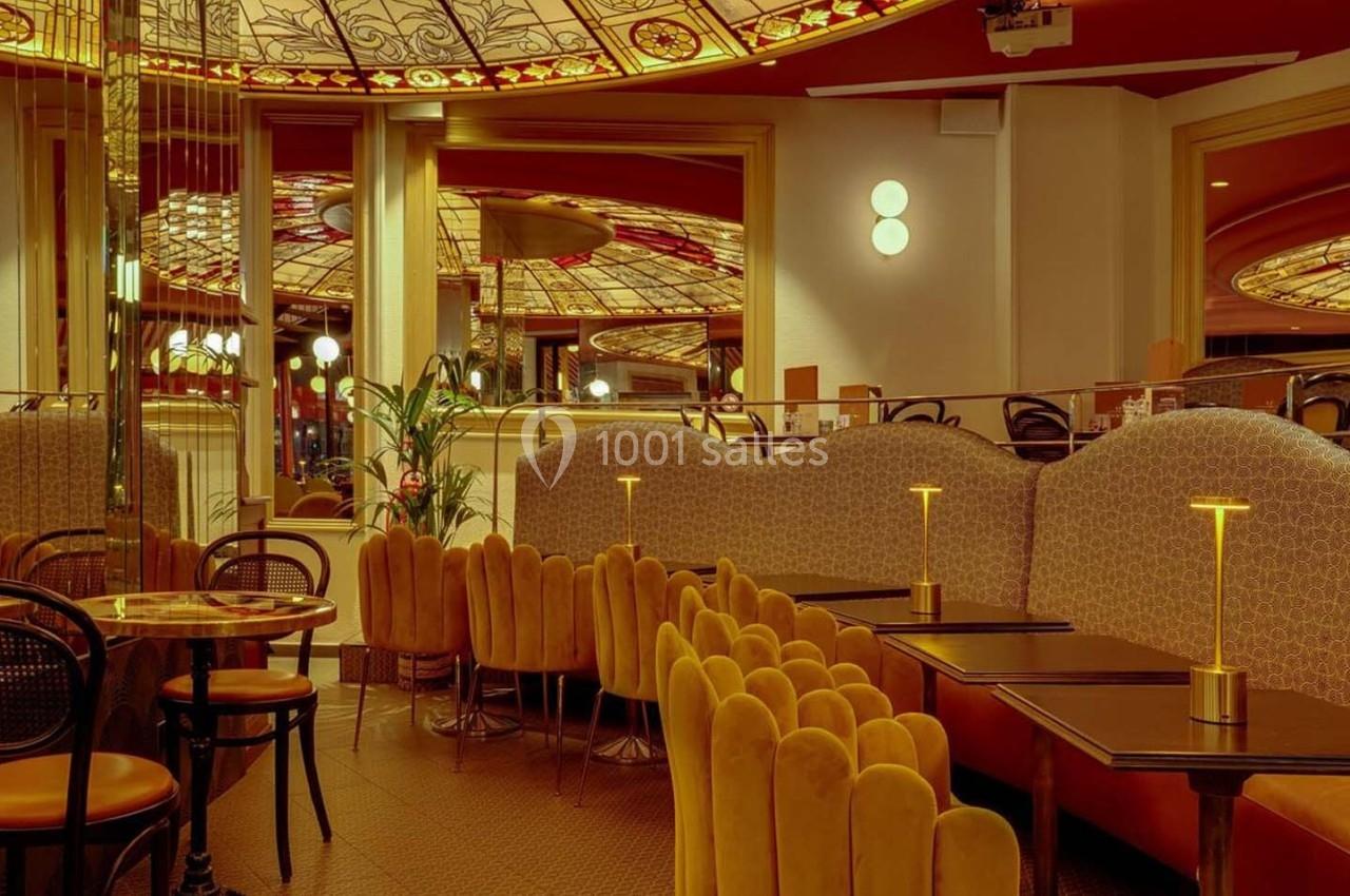 Salle de restaurant élégante avec banquettes jaunes, chaises en velours et plafond décoré de vitraux colorés.