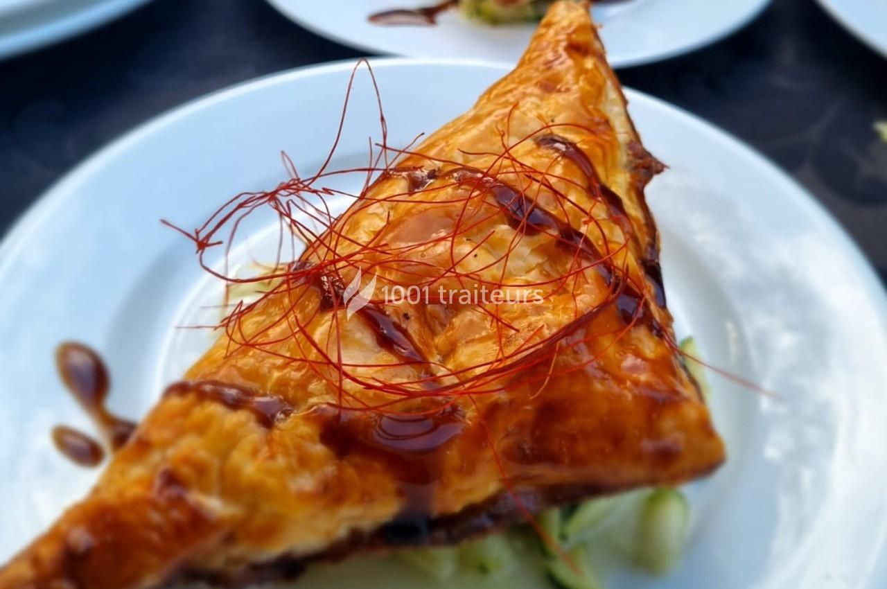 Feuilleté doré garni, nappé de sauce et décoré de filaments rouges, servi sur une assiette blanche.