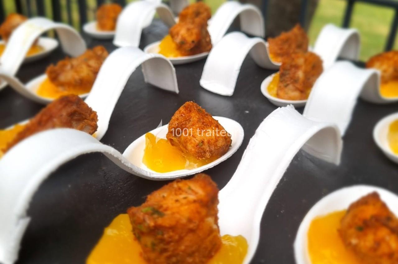 Bouchées de poulet croustillant servies sur des cuillères avec une sauce jaune, présentées sur un plateau noir.