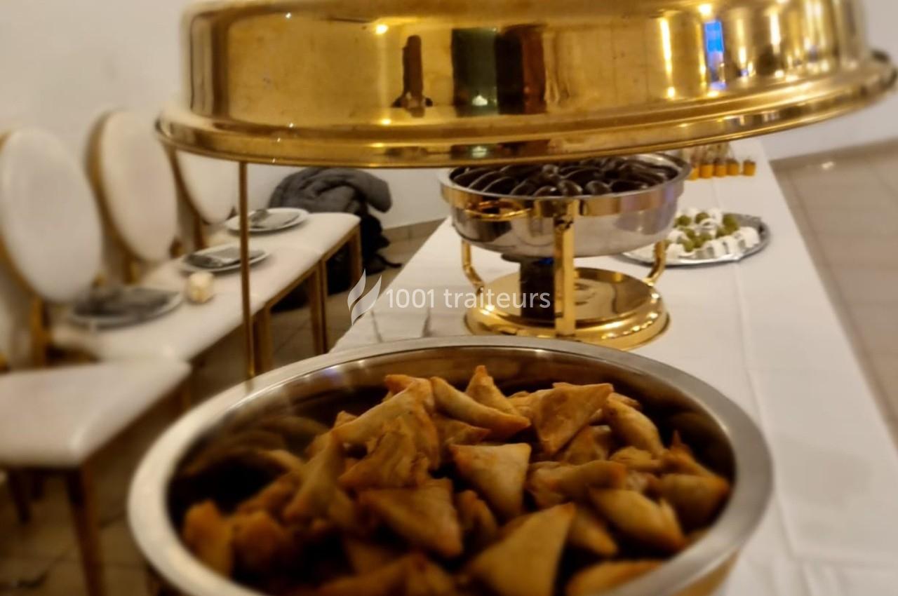Assortiment de samoussas dans un plat en métal, avec d'autres mets disposés sur une table de buffet.