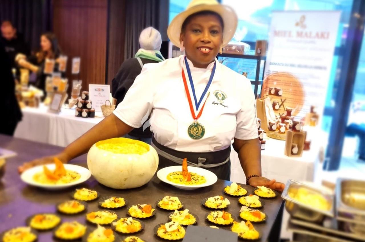 Une cheffe en tenue professionnelle présente des amuse-bouches disposés sur un plateau, avec une citrouille creuse en…