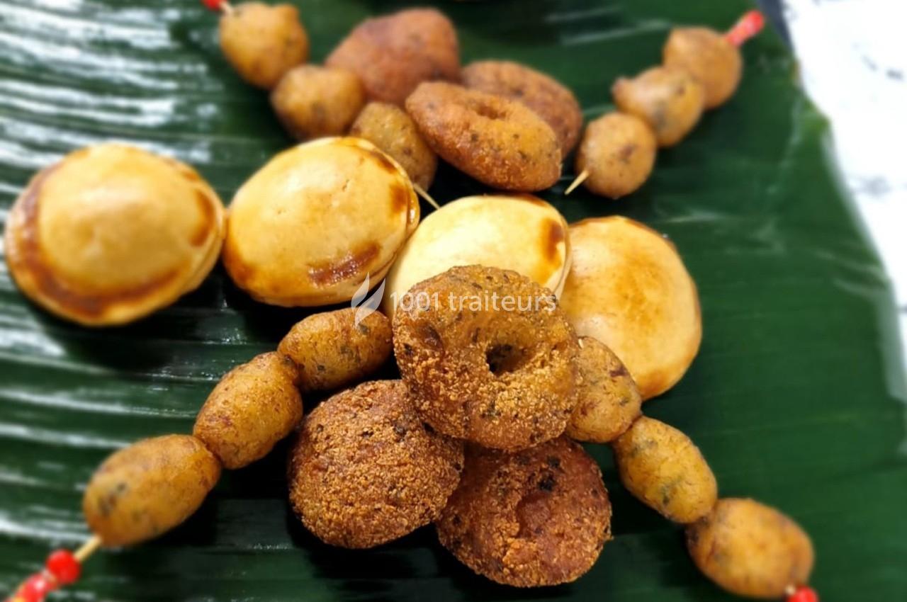 Assortiment de beignets et brochettes de snacks frits disposés sur une feuille de bananier.