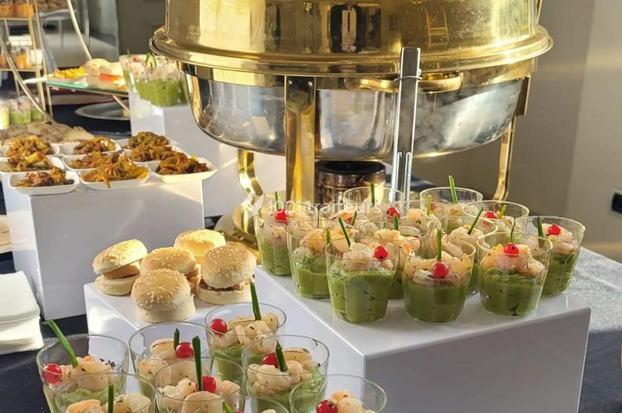 Buffet avec verrines d'avocat et crevettes, mini burgers et plats variés présentés sur une table élégante.