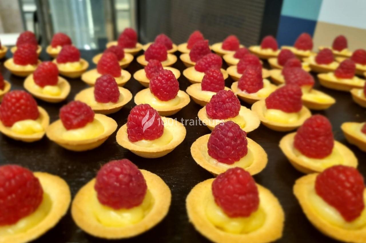 Tartelettes garnies de crème pâtissière et surmontées de framboises fraîches, disposées sur une table.