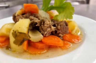 Huîtres gratinées garnies de fromage et épices, présentées sur un plateau en bois, avec légumes en arrière-plan.
