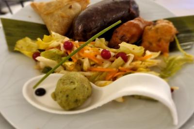 Huîtres gratinées garnies de fromage et épices, présentées sur un plateau en bois, avec légumes en arrière-plan.