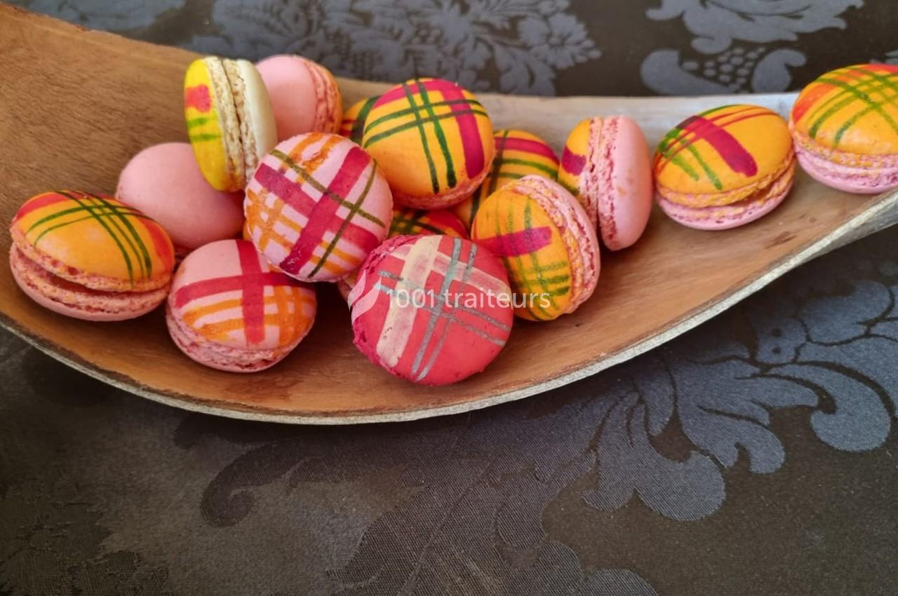 Macarons colorés avec motifs à carreaux disposés dans une cuillère en bois sur une nappe à motifs floraux.