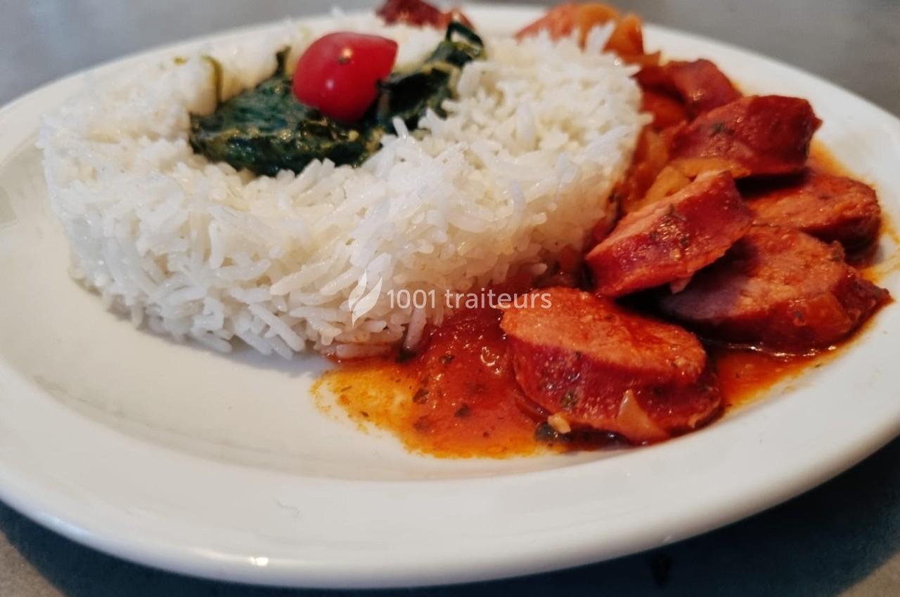 Assiette de riz blanc accompagné de morceaux de saucisse en sauce tomate et de légumes verts.