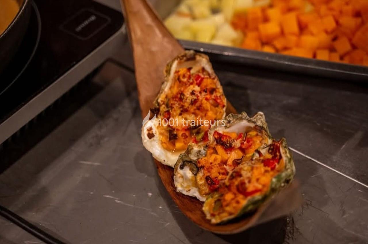 Huîtres gratinées garnies de fromage et épices, présentées sur un plateau en bois, avec légumes en arrière-plan.