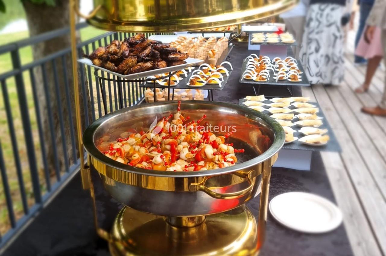 Buffet en extérieur avec des plats variés, incluant brochettes, amuse-bouches et grillades, disposés sur des tables.