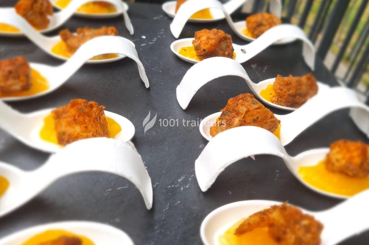 Cuillères en porcelaine blanche contenant des bouchées de viande sur une sauce orange, disposées sur une table noire.