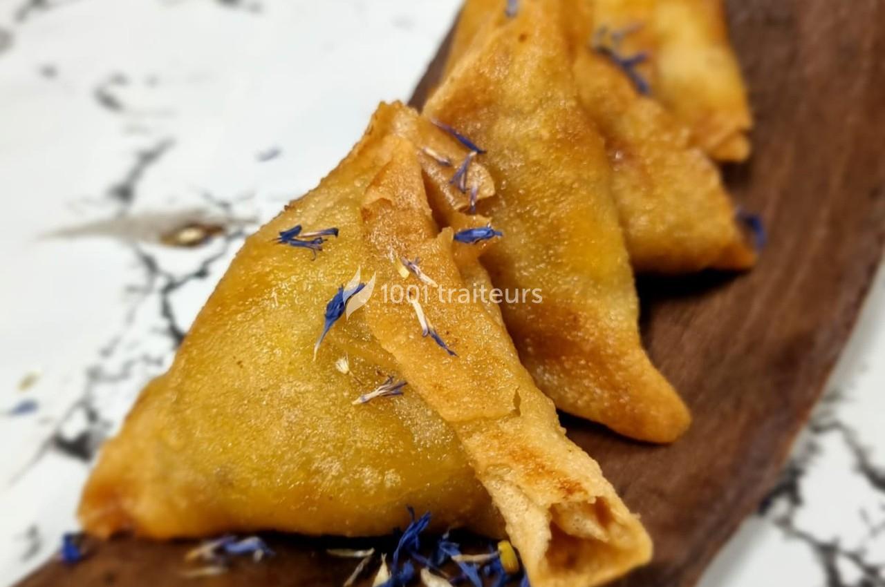 Samosas dorés garnis de fleurs comestibles bleues, disposés sur un plateau en bois.