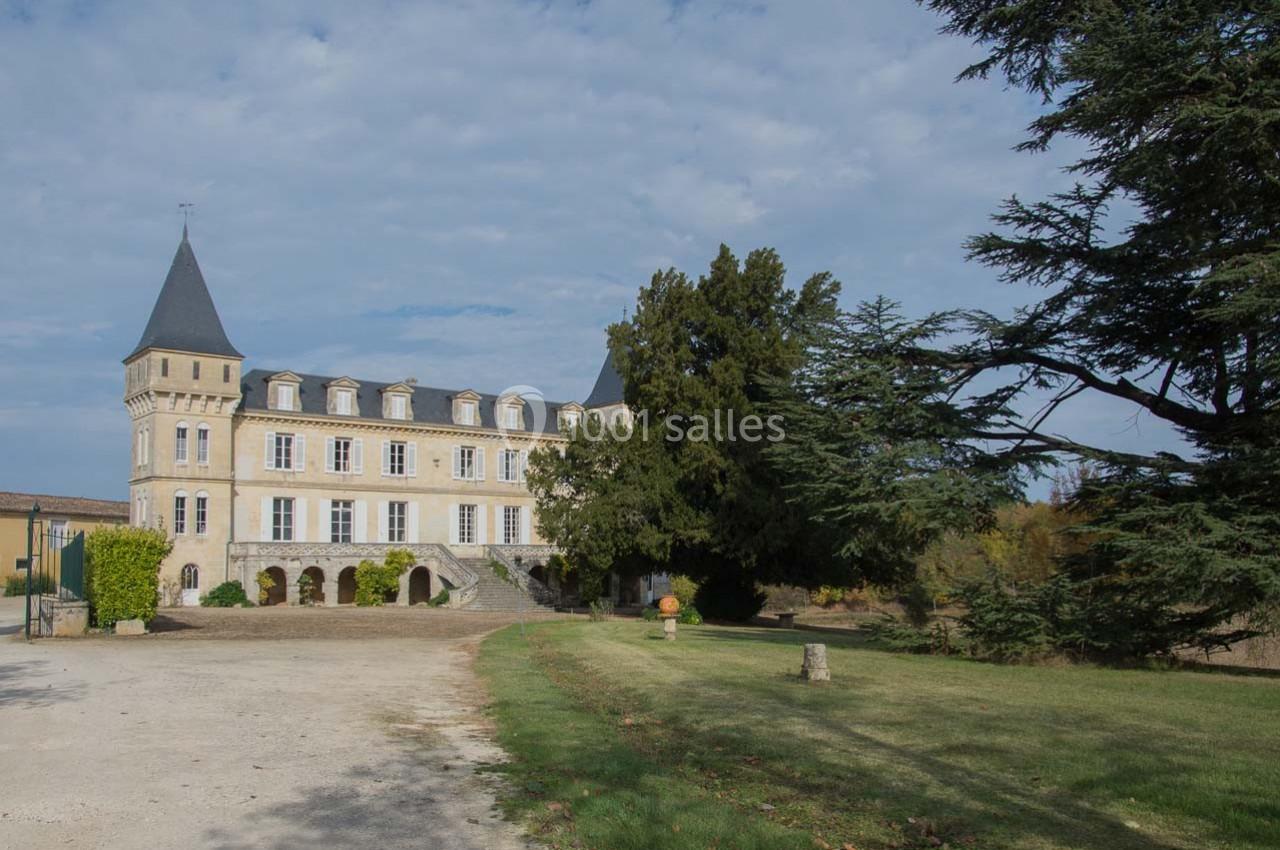 Façade d'un château avec tours, entouré d'arbres et d'une pelouse, sous un ciel partiellement nuageux.