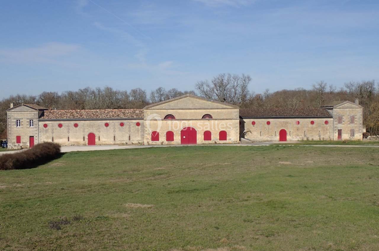 Bâtiment en pierre avec portes et fenêtres rouges, entouré de pelouse et d'arbres sous un ciel dégagé.