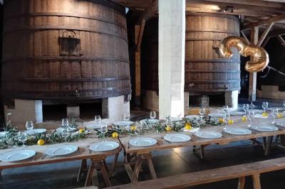 Grande table dressée avec vaisselle et décoration florale dans une salle voûtée avec tonneaux et cuves en arrière-plan.