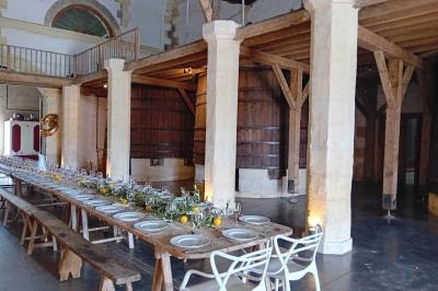 Grande table dressée avec vaisselle et décoration florale dans une salle voûtée avec tonneaux et cuves en arrière-plan.