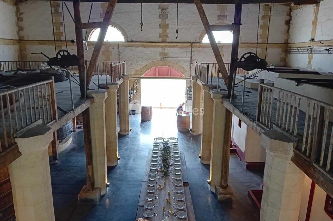 Intérieur d'un bâtiment en pierre avec une grande table dressée au centre, entourée de balcons en bois.