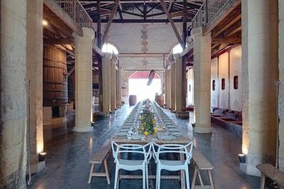 Grande table dressée avec vaisselle et décoration florale dans une salle voûtée avec tonneaux et cuves en arrière-plan.