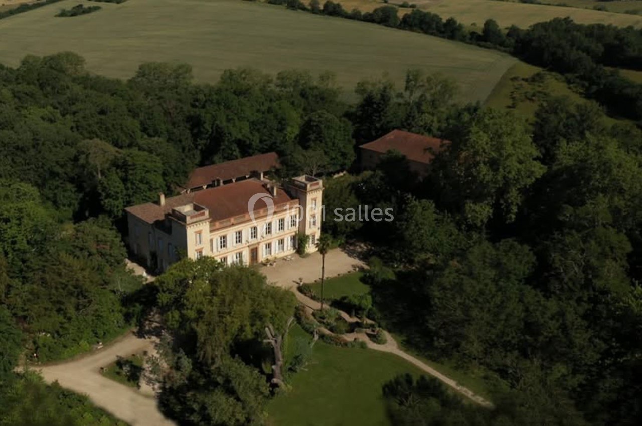 Vue aérienne d'un grand bâtiment historique entouré de verdure et de champs, avec une allée menant à l'entrée.