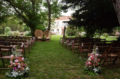 Grande table dressée avec vaisselle élégante, pains individuels et décoration florale, sous une terrasse en bois ouverte sur…