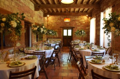 Grande table dressée avec vaisselle élégante, pains individuels et décoration florale, sous une terrasse en bois ouverte sur…