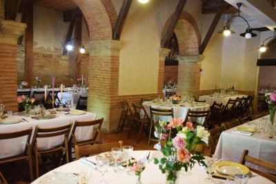 Grande table dressée avec vaisselle élégante, pains individuels et décoration florale, sous une terrasse en bois ouverte sur…