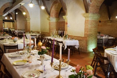 Grande table dressée avec vaisselle élégante, pains individuels et décoration florale, sous une terrasse en bois ouverte sur…