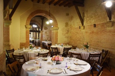 Grande table dressée avec vaisselle élégante, pains individuels et décoration florale, sous une terrasse en bois ouverte sur…
