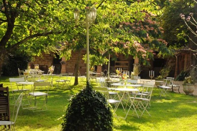 Grande table dressée avec vaisselle élégante, pains individuels et décoration florale, sous une terrasse en bois ouverte sur…