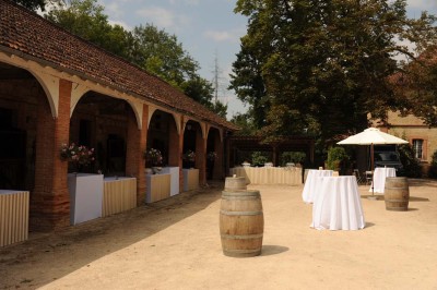 Grande table dressée avec vaisselle élégante, pains individuels et décoration florale, sous une terrasse en bois ouverte sur…