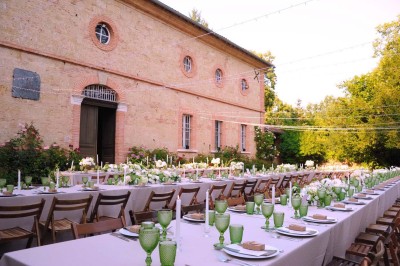 Grande table dressée avec vaisselle élégante, pains individuels et décoration florale, sous une terrasse en bois ouverte sur…