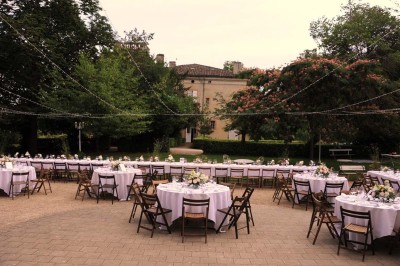 Grande table dressée avec vaisselle élégante, pains individuels et décoration florale, sous une terrasse en bois ouverte sur…