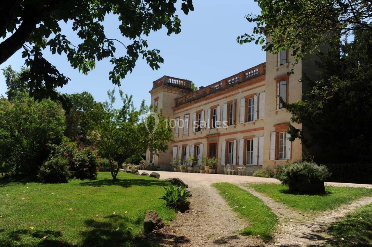 Allée bordée de verdure menant à une grande maison de style ancien entourée d'arbres et de jardins.