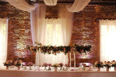 Grande table dressée avec vaisselle élégante, pains individuels et décoration florale, sous une terrasse en bois ouverte sur…